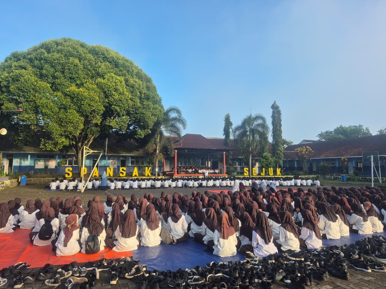 Aerial view of Indonesian school with golden roofs, green sports court, and surrounding forest.